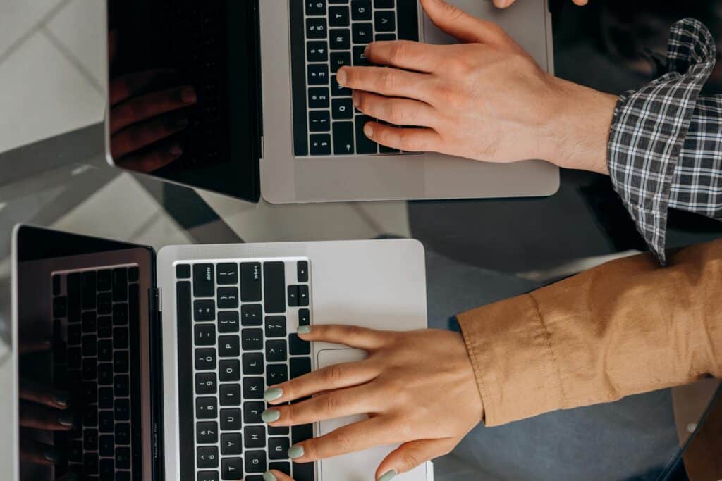 Two hands typing on two laptops