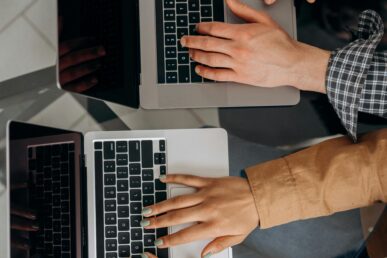 Two hands typing on two laptops