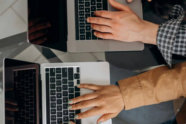 Two hands typing on two laptops